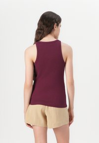 Maroon tank top in ribbed fabric, sleeveless design, round neckline, paired with light beige shorts, smooth texture, fitted silhouette.