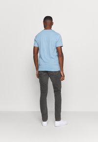 Světle modré tričko s krátkým rukávem, šedé džíny s úzkým střihem, bílé tenisky. Jednoduchý design na zádech s minimálním zdobením a rovný lem.