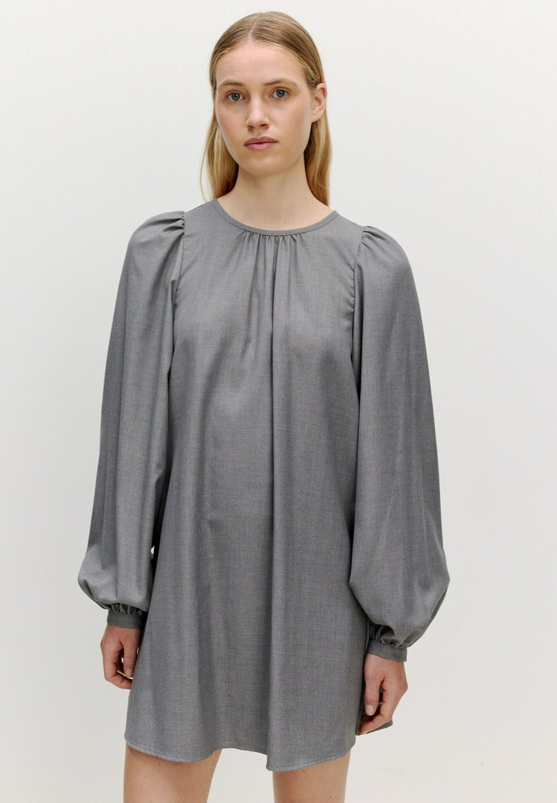 Graues Langarmkleid mit gerafften Schultern und rundem Ausschnitt, aus strukturiertem Stoff gefertigt. Der Saum endet über dem Knie.