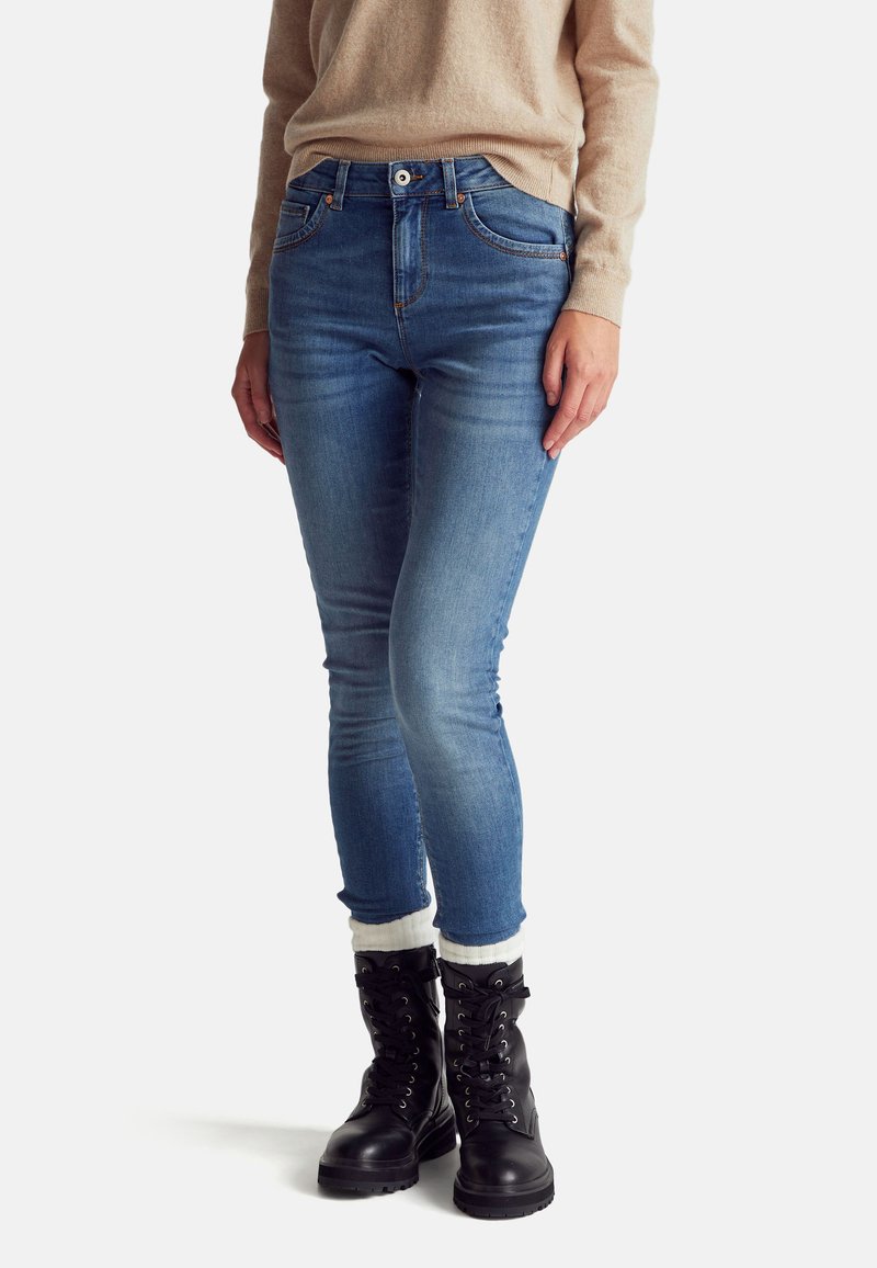 Vaqueros ajustados de color azul con una cintura alta, con un ligero desvanecimiento y dos bolsillos frontales. Combinados con unas botas de tobillo negras con cordones y calcetines blancos.