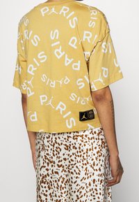 Gul bomullströja med vit text "PARIS" över hela ytan och Jordan-logotypen. Har en kortad form och en svart etikett i fållen.