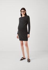 Fekete kötött ruha hosszú ujjakkal és testhez simuló fazonnal. Fekete cipőkkel kombinálva ezüst kiegészítőkkel és téglalap alakú napszemüveggel.