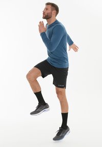 Long-sleeve blue athletic top, black shorts, black socks, and gray running shoes. Active pose with a raised knee, textured fabric visible.