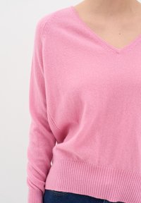 Różowy dziergany sweter z dekoltem w serek, długimi rękawami i ściągaczem na dole; miękka tekstura i lekki materiał, odpowiedni do codziennego noszenia.