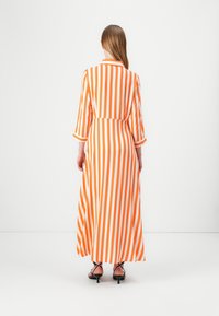Pitkä mekko, jossa on oransseja ja valkoisia pystyraitoja, kauluksellinen pikkupaita ja kolme neljännesosaa hihat, valmistettu kevyestä kankaasta.