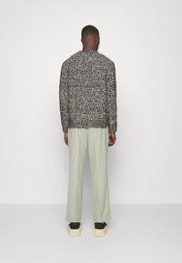 Suéter texturizado en blanco y negro con un corte holgado, combinado con pantalones de pierna ancha en verde claro y zapatillas de plataforma negras.