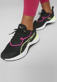 Czarne buty sportowe z siateczkową tkaniną, różowymi i neonowo żółtymi akcentami oraz teksturowaną podeszwą. Projekt sznurowany z wyściełanym kołnierzem dla komfortu.