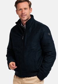 Navy blue jacket with a smooth, textured finish, high collar, zip closure, chest pocket, and logo detail on the left shoulder.