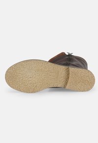 Brown leather ankle boot with a textured rubber sole, side zipper, and a soft inner lining. The outsole is beige with a patterned grip.