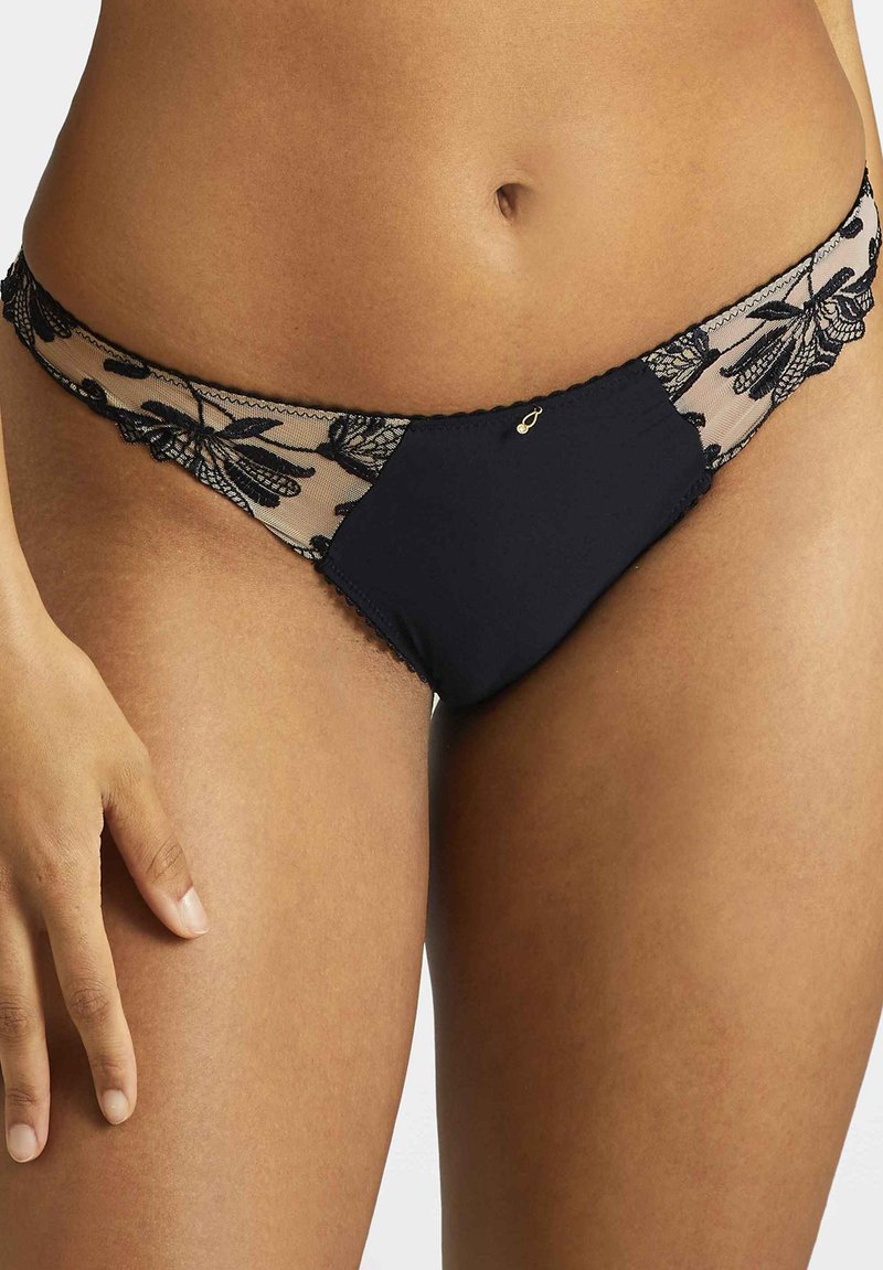 Bas de bikini noir avec superposition en dentelle présentant un motif floral. Tissu lisse à l'avant, dentelle transparente sur les côtés, et bords délicats en forme de vague.
