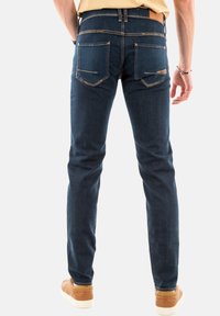 Jeans oscuros de corte slim hechos de mezclilla, con bolsillos traseros con costuras decorativas y un detalle de cuero marrón en la cinturilla.