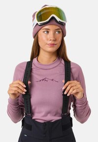 Roze geribbelde longsleeve met bergafbeelding, zwarte bretels en een zwarte buitenbeanie. Voorzien van reflecterende skibril met gele lenzen.