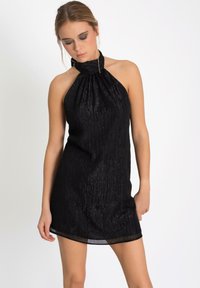 Robe noire à dos nu avec un col froncé, fabriquée en tissu texturé et scintillant. Longueur courte avec une silhouette ajustée, ourlet lisse.