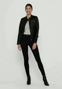 Zwarte leren jas met een getailleerd ontwerp, voormet een rits en twee borstzakken. Gecombineerd met een grijze crop top en zwarte leggings.