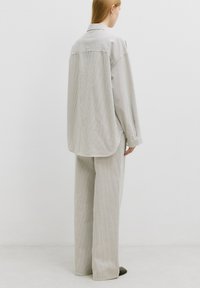 Gestreepte shirt en wijde broek in licht taupe en crème. Zachte katoenen stof met een losse fit en een ontspannen kraag. Subtiele verticale strepen.