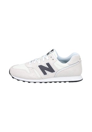 Zapatilla New Balance blanca y gris claro con logo "N" negro, cordones blancos y suela de goma negra, vista de lado sobre un fondo blanco.