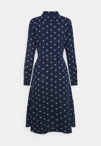 Námořnické šaty vyrobené z látky s bílými diamantovými vzory. Dlouhé rukávy a límečkový výstřih. Rozšířený lem.