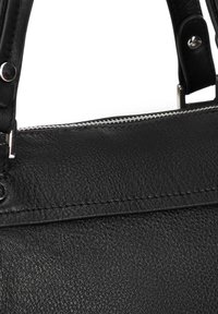 Nahaufnahme einer schwarzen Lederhandtasche, die die Textur, die Nähte, den silbernen Reißverschluss und den Riemen mit Metalldetail-Nieten zeigt.