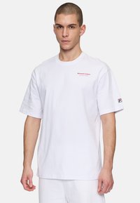 Hvid bomulds T-shirt med korte ærmer og rund hals. Har rødt tekst på brystet og et logo på ærmet. Løs pasform.
