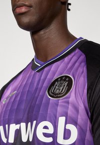 Μπλούζα αθλητική με μωβ και μαύρες ρίγες και V-λαιμόκοψη, με λογότυπο στο στήθος και λευκά γράμματα στο εμπρός μέρος. Ορατό υφασμένο ύφασμα.