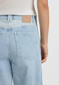 Jasnoniebieskie dżinsy z denimu z dwiema tylnymi kieszeniami, skórzaną metką w pasie oraz prostym krojem nogawki. Minimalne przetarcia widoczne.