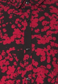 Schwarzes Hemd mit rotem Blumenmuster, das einen Kragen und eine knöpfbare Vorderseite aufweist. Das Material scheint glatt und leicht zu sein, mit einem strukturierten Stoffdesign.