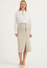 Beige gestreifte Bleistift-Rock mit vorderem Schlitz, seitlichen Taschen und schwarzen Knöpfen. Kombiniert mit einer weißen Bluse und weißen Absätzen.