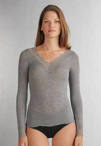 Grijs langemouwen shirt van zachte stof met een diepe V-hals en delicate kantafwerking bij de halslijn en manchetten. Heeft een aangesloten silhouet.