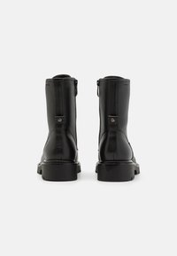Black leather ankle boots with a textured finish, smooth zipper closure, and chunky low heel; features a circular metallic accent on the heel.