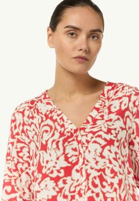 Czerwono-biała bluzka w kwiatowy wzór z dekoltem w serek, z długimi rękawami, wykonana z lekkiego materiału.