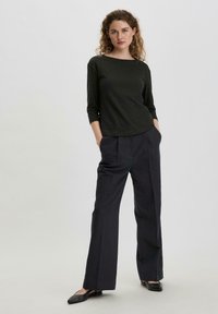 Schwarzes Langarmoberteil mit rundem Ausschnitt, kombiniert mit hochtaillierten, weit geschnittenen dunklen Hosen und flachen schwarzen Schuhen. Einfaches, maßgeschneidertes Design.