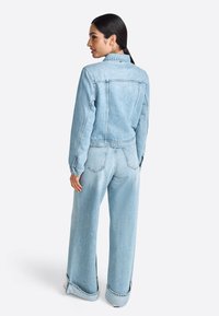 Giacca di jeans azzurro chiaro e jeans a gamba larga con un taglio rilassato. Caratteristiche includono tasche cucite e polsini arrotolati.