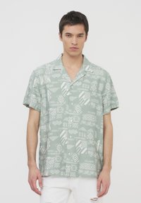 Camicia a maniche corte in tessuto verde chiaro con motivi geometrici bianchi, caratterizzata da un colletto a punte e chiusura con bottoni.