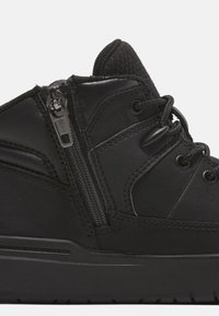 Botte noire à la cheville avec une finition texturée, fermeture éclair et détails en dentelle. La semelle est plate avec un bord légèrement surélevé pour un meilleur soutien.