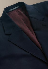 Marineblauer Anzugjacke mit feiner Textur, ausgestattet mit einem burgunderfarbenen, gemusterten Futter, das am Kragen und Revers sichtbar ist. Schlichtes Design, keine sichtbaren Beschläge.