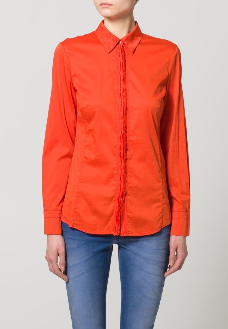 Camicia rossa con bottoni, dotata di una patta anteriore testurizzata e maniche lunghe, realizzata in un tessuto leggero. Abbinata a jeans blu.