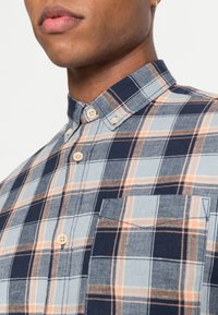 Camicia con bottoni caratterizzata da un motivo a quadri blu e bianchi con dettagli arancioni. Design con colletto, taschino sul petto e tessuto texture.