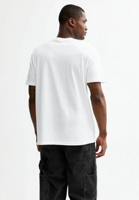 Camiseta blanca de algodón con cuello redondo, manga corta y corte holgado, combinada con pantalones cargo negros con bolsillos laterales.