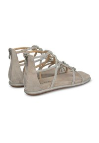 Sandalias de ante beige con tiras trenzadas y acentos metálicos. Cierre de cremallera en la parte trasera, suela plana y textura suave. Diseño de punta abierta.