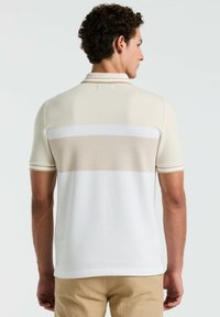 Korte mouwen polo shirt in licht beige met witte en tan horizontale strepen. Bevat een kraag en ribgebreide boorden. Gecoate stof.