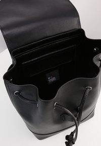 Sac seau en cuir noir avec une texture lisse, fermeture à cordon, et poches internes. Comprend une étiquette logo à l'intérieur.