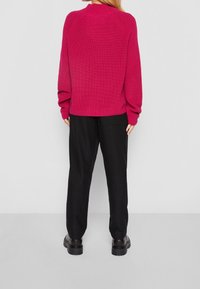 Fuksjowy sweter z dzianiny z raglanowymi rękawami, dopasowany krój i prążkowana tekstura, w połączeniu z luźnymi czarnymi spodniami i masywnymi czarnymi botkami.