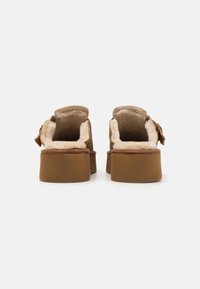 Brown suede shoes with a plush interior, featuring a chunky platform sole and open back design. Hardware accents are minimal.