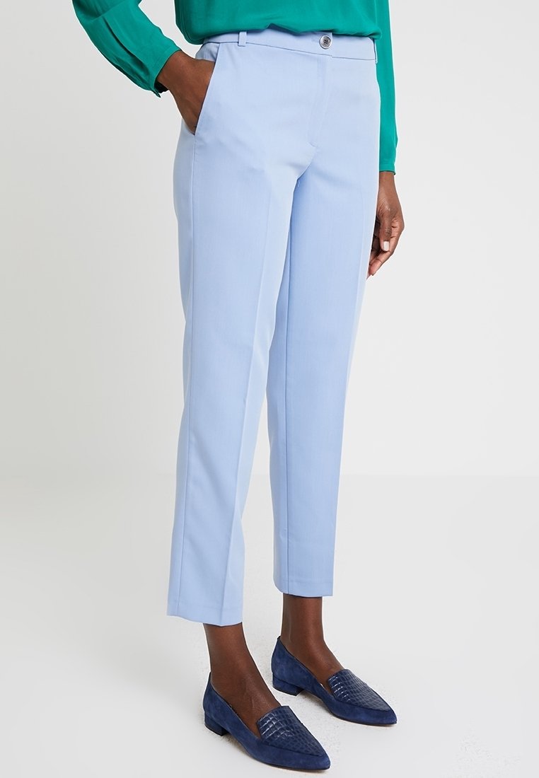 Jasnoniebieskie dopasowane spodnie o prostym kroju, z bocznymi kieszeniami i zapięciem na guzik. Zestawione z ciemnoniebieskimi butami wsuwanymi.