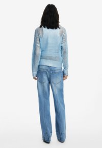 Hellblaues gestricktes Sweatshirt mit lockerer Passform und strukturiertem Muster, kombiniert mit weit geschnittenen hellblauen Jeans aus Denim mit Gesäßtaschen.