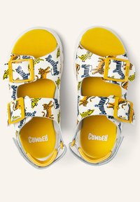 Children’s white sandals with yellow insoles, two yellow buckles each, and colorful animal prints including zebras and tigers.