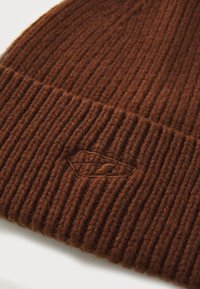 Brown knitted beanie with ribbed texture and a folded cuff. Features an embroidered logo in a matching brown shade. Soft wool material.