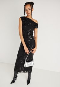 Melnā oficiālā kleita ar teksturētām ziedu apdare, pieguļošs siluets, caurredzama apakšmala, kombinēta ar sudraba somu un ceļgalu augstiem stiletto zābakiem.