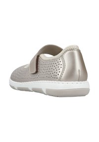 Light beige shoe with a perforated design, adjustable strap, white sole, rounded shape, and stitched accents. Textured back panel.
