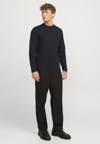 Donkerblauwe gebreide trui met een ronde halslijn en lange mouwen, gecombineerd met zwarte wijduitlopende broek en zwarte veterschoenen.